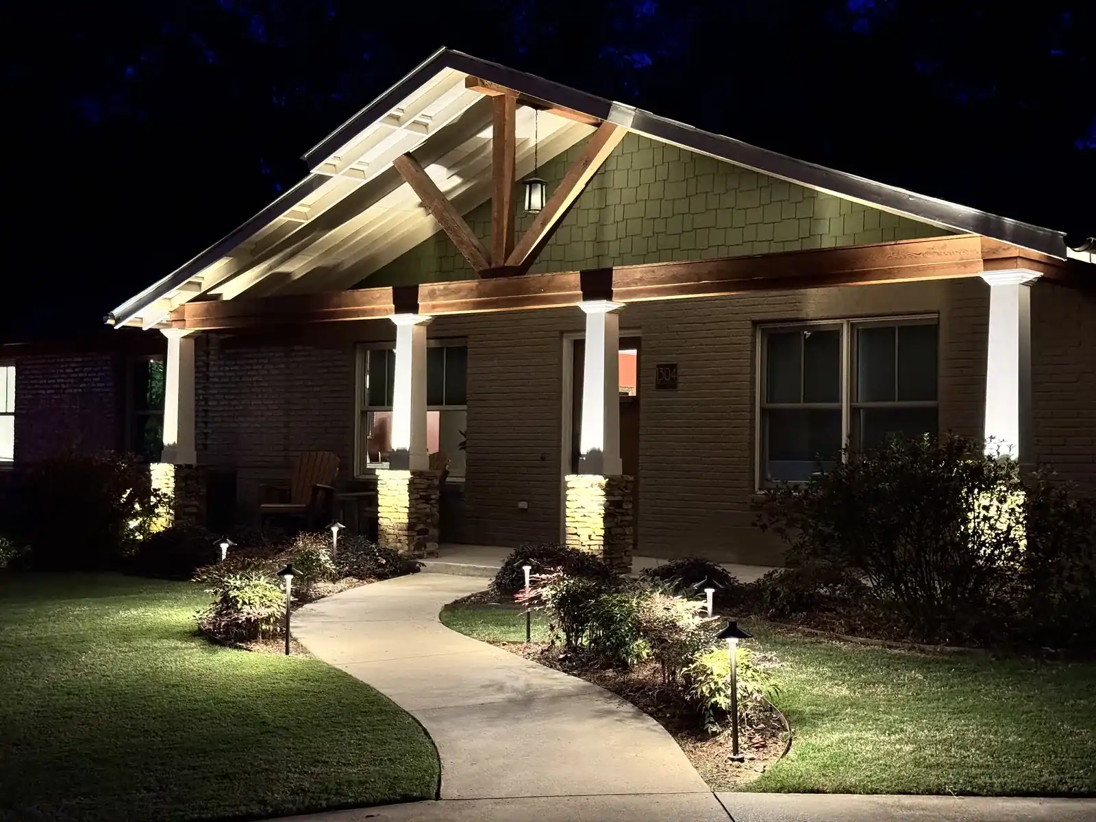 Craftsman house with lit columns and path lights along a curved front walk at night