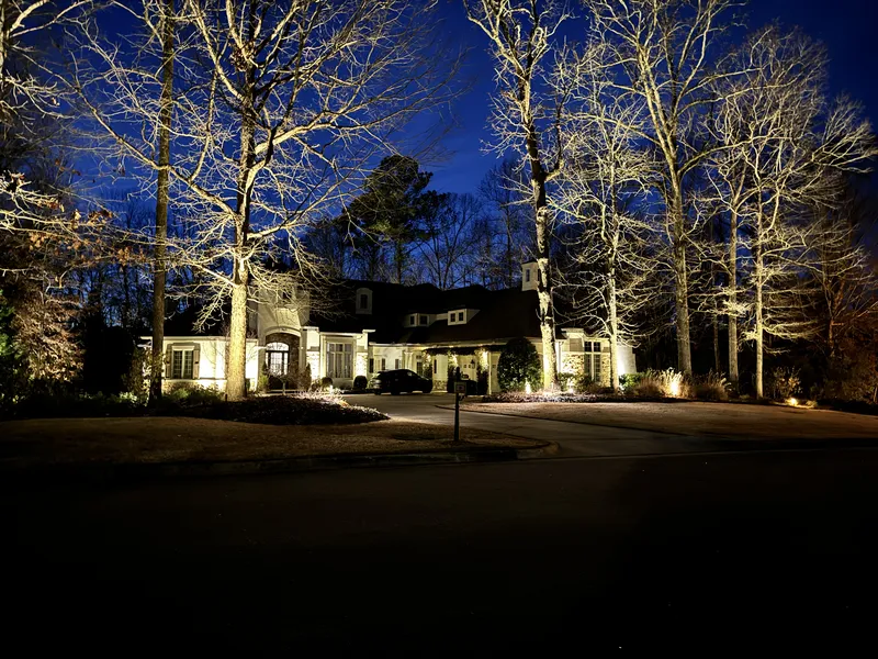 Large home at night with uplit trees and warm facade lighting across a wide lawn