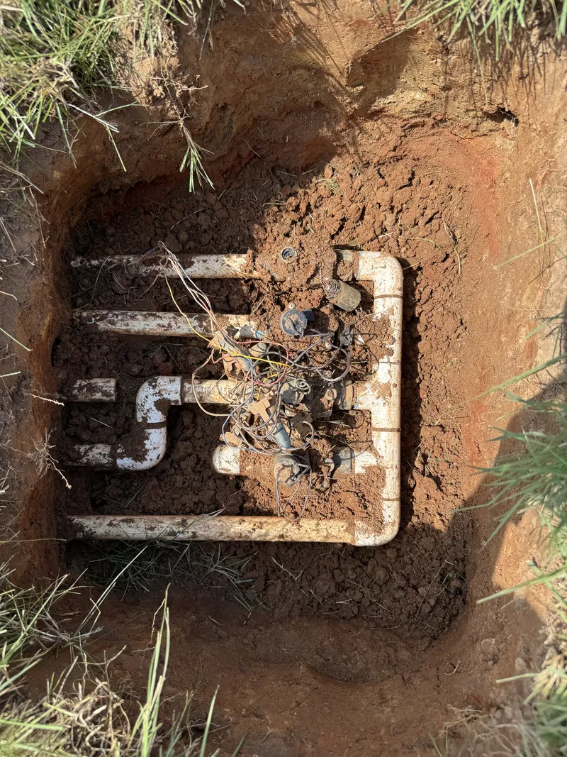 White PVC valve manifold assembled in a hole in red clay soil