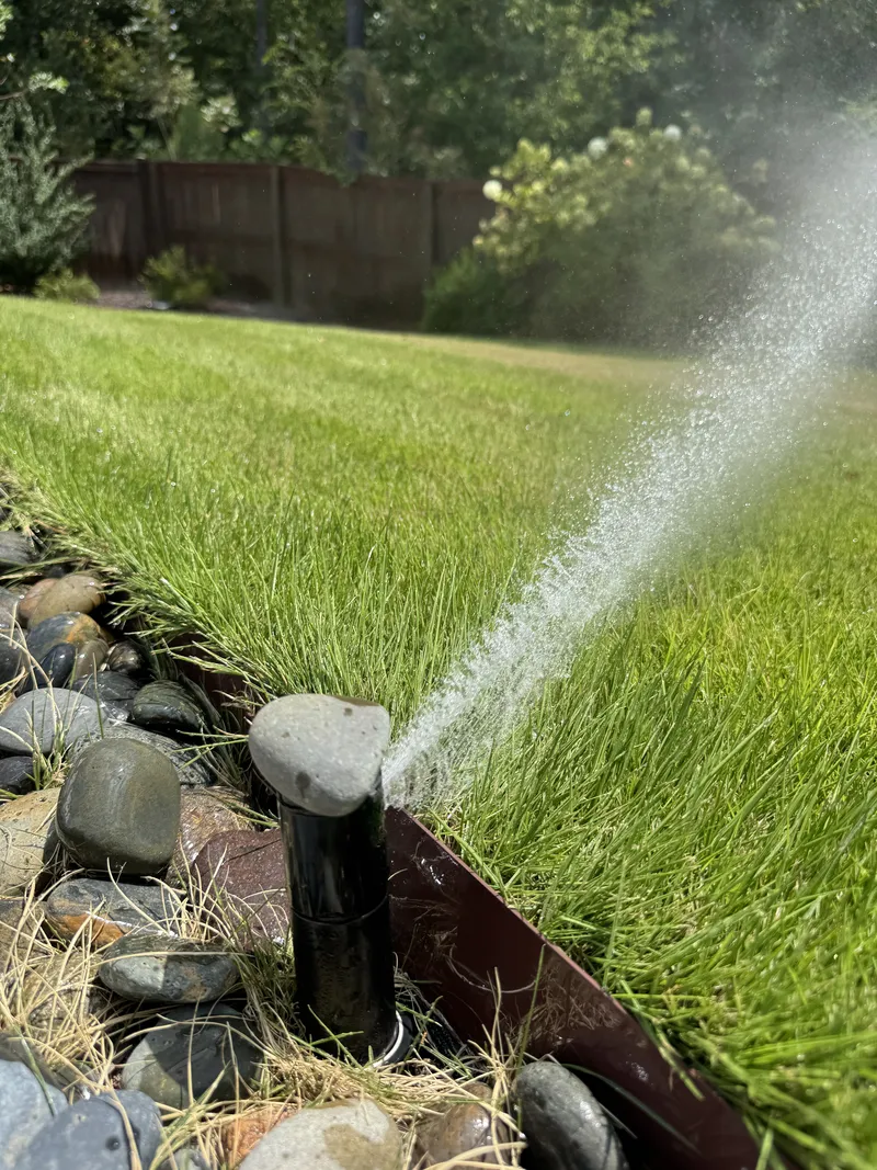 Rotor head spraying lawn beside a river rock border and steel edging