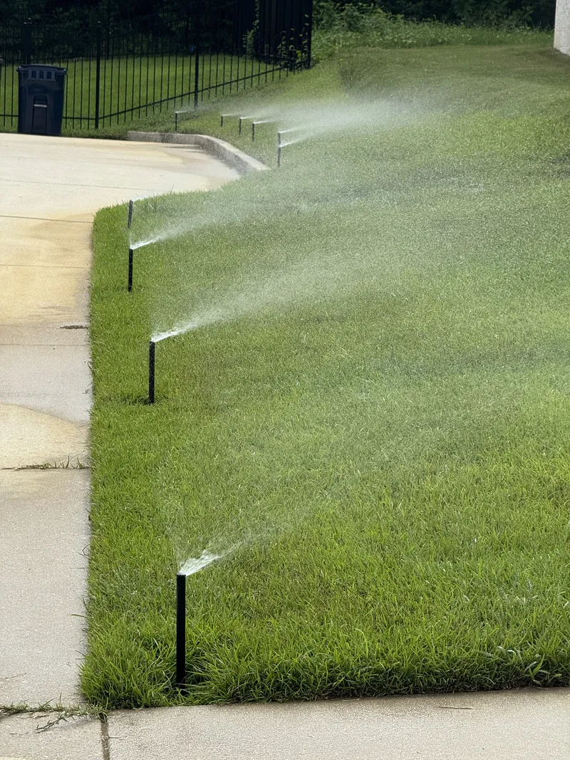 Row of pop-up spray heads watering green grass beside a curved sidewalk