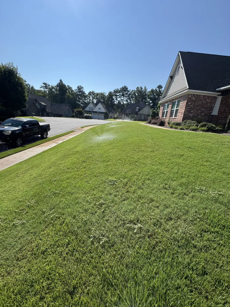 Sprinklers watering a sloped green front lawn of a brick home