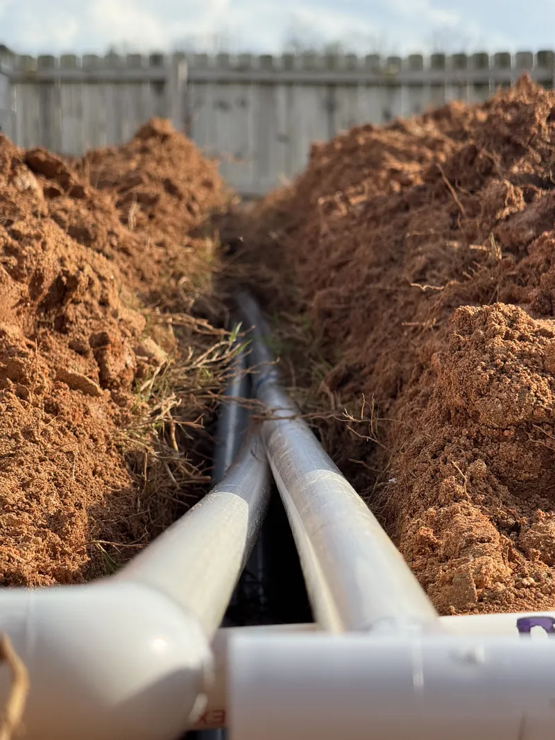 Open trench in red clay with new PVC irrigation pipe being laid